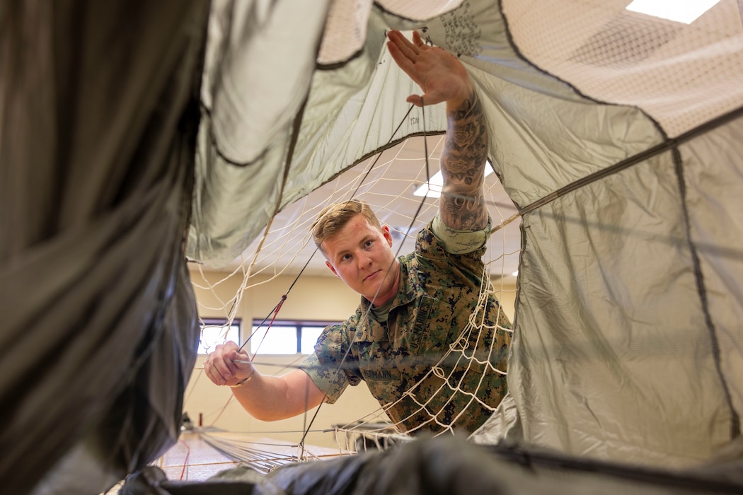 U.S. Marine Corps Cpl. Ashton Permann, an airborne and air delivery specialist with 2nd Distribution Support Battalion, Combat Logistics Regiment 2, 2nd Marine Logistics Group, inspects a parachute at Marine Corps Base Camp Lejeune, April 30, 2025.Permann was selected by his command due to his constant dedication to the mission success while serving as section leader, jumpmaster and embarkation chief for 1st Platoon Air Distribution Company which is a senior noncommissioned officer billet that includes providing logistical planning, management, and the execution of Air Distribution Company operations. As a Jumpmaster, Permann has conducted, planned, executed, and supervised over 12 cargo and personnel drops within the past three months. Each week, 2nd MLG recognizes one outstanding Marine or Sailor that goes above and beyond in their duties and embodies the qualities of an outstanding service member. (U.S. Marine Corps photo by Lance Cpl. Isabella Ramos)