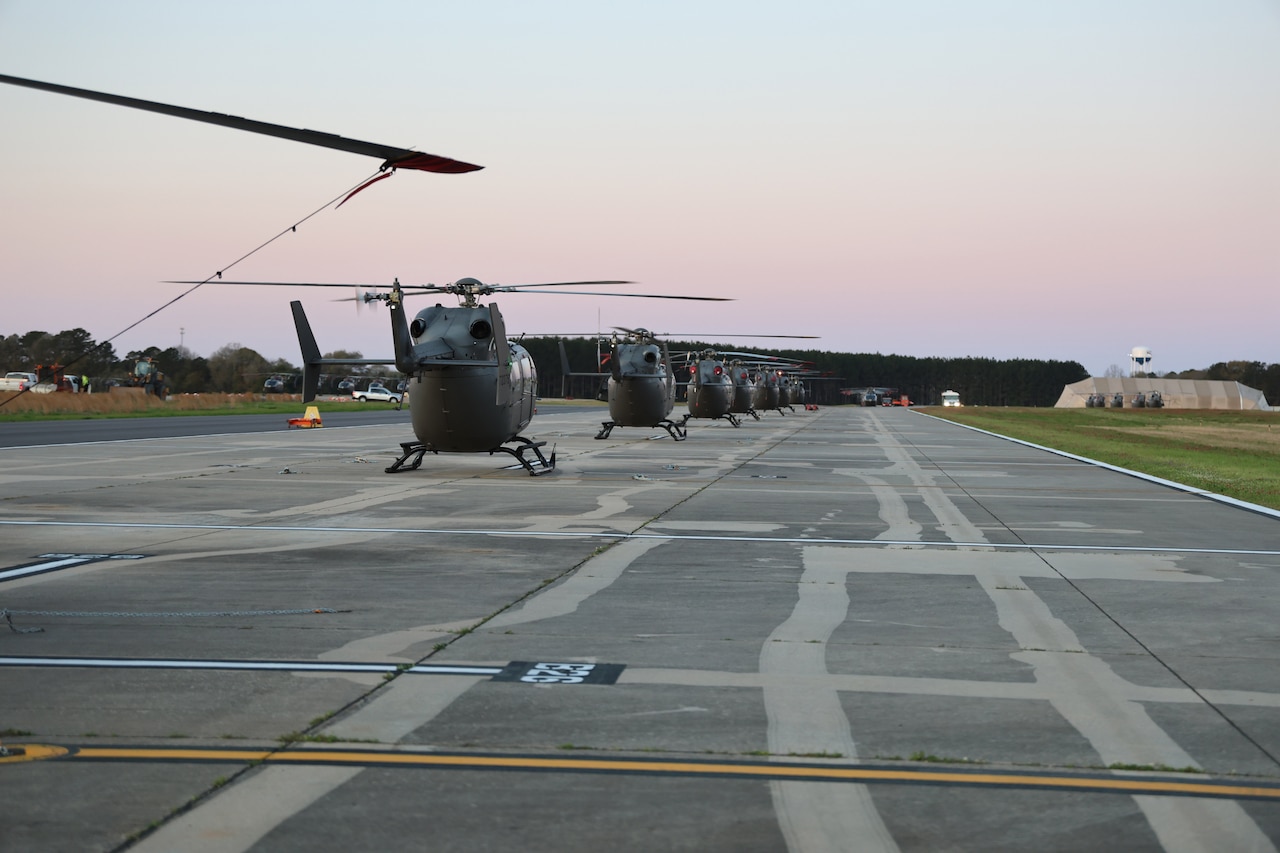 Helicopters, shown from behind, sit in a line on a flight line.