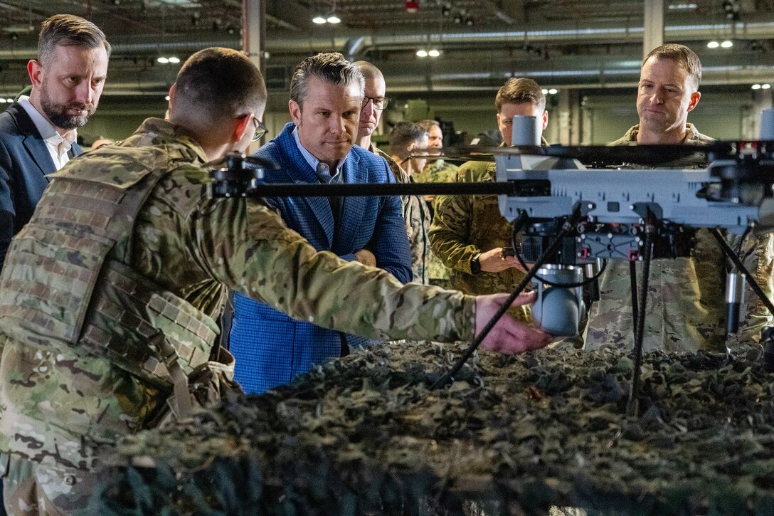 Defense Secretary looks at a drone on a table while standing with his Polish counterpart and U.S. soldiers.