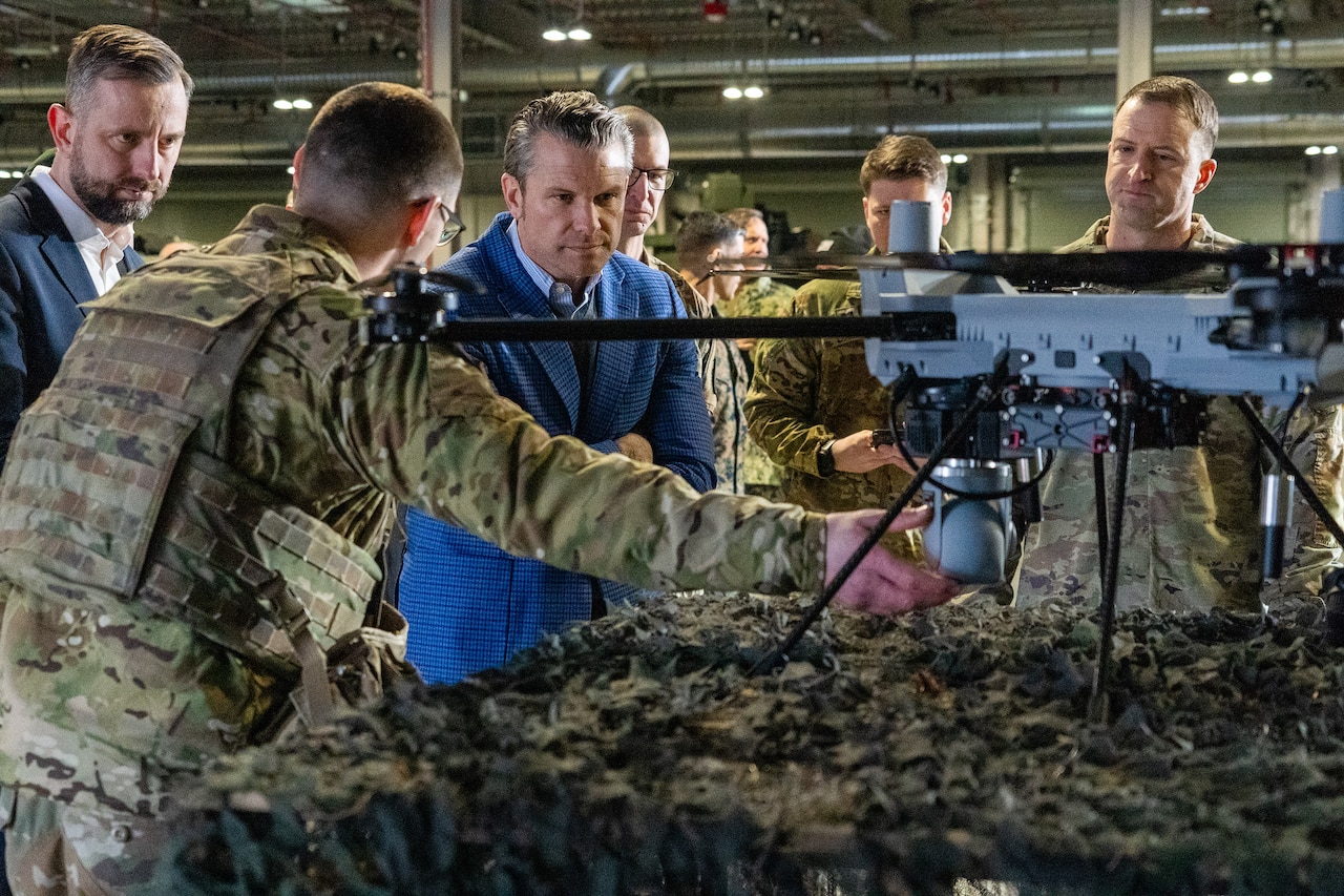 Defense Secretary looks at a drone on a table while standing with his Polish counterpart and U.S. soldiers.