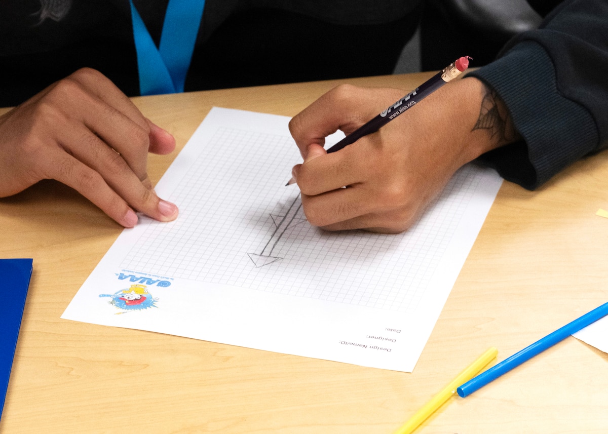 A pair of hands holds a pencil and draws on graph paper.