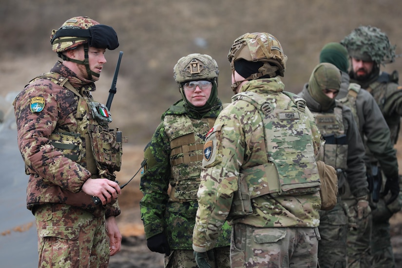 Italian Army OR-8 Eduard Raduna (left,) Canadian Army Capt. Chelsea Stephen (center,) U.S. Army Capt. Mark Fisher, commander of Bravo company, 10th Brigade Engineer Battalion, 1st Armored Brigade Combat Team, 3rd Infantry Division, in support of Task Force Iron, discusses events during Verboom in Ādaži, Latvia, March 18, 2025. Exercise Verboom is a multinational training exercise with the goal of enhancing soldiers from varying nations interoperability and effectiveness on the removal of anti-personnel obstacles. Task Force Iron's mission is to engage in multinational training and exercises across the continent to increase lethality, while strengthening partnerships with our NATO allies and regional security partners. The task force provides combat-credible forces to V Corps, America’s only forward-deployed corps in Europe. (U.S. Army photo by Spc. Trevor Wilson)
