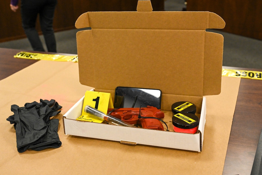 A cell phone, prop gun, and powders used for finding fingerprints are boxed up near the end of the Law Day demonstration at Altus Air Force Base, Oklahoma, May 1, 2025. The mock crime scene set–up gave students a closer look at how and where objects are found can become clues during a crime scene investigation. (U.S. Air Force photo by Senior Airman Kari Degraffenreed)