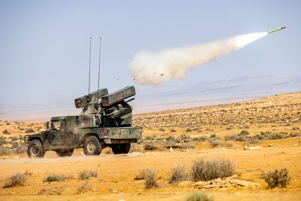 A missile is launched from a military vehicle over arid terrain and into a field, leaving behind smoke.