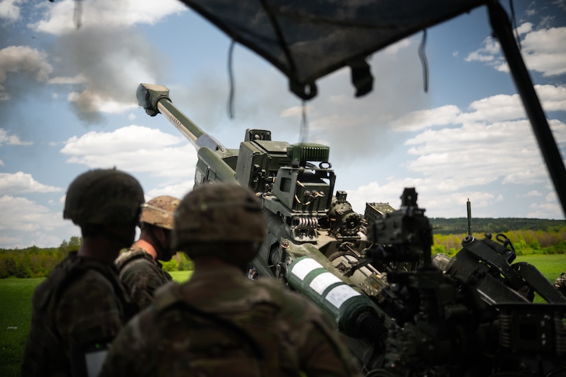 Three soldiers in camouflage uniforms fire a large military weapon.