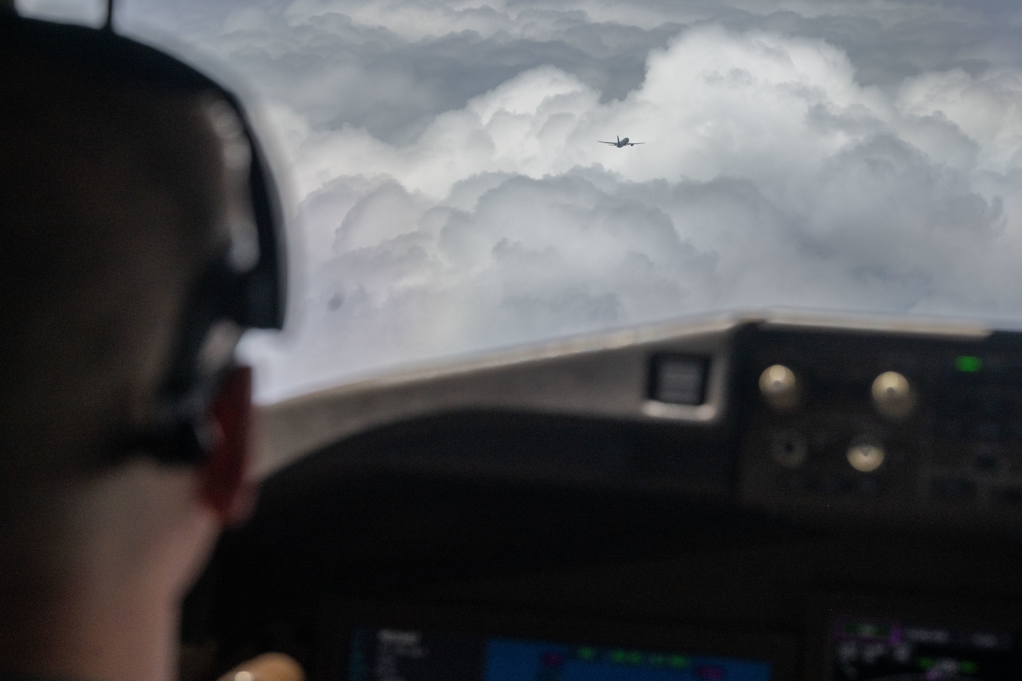 A pilots looks out a window at another KC-46 tanker in the sky, off in the distance.