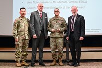 U.S. Army Sgt. Maj. Andy Yoshimura, U.S. Army Training and Doctrine Command quality assurance evaluator Sergeant Major (left), Dr. John Plifka, TRADOC quality assurance director, Sgt. 1st Class Gerald Funk, Quality Assurance Evaluator of the Year, and Michael Formica, Executive Deputy to the TRADOC Commanding General, stand before attendees of the inaugural U.S. Army quality assurance program forum as Funk is named the quality assurance evaluator of the year at Fort Eustis, Va. March 4, 2025. (Courtesy photo)