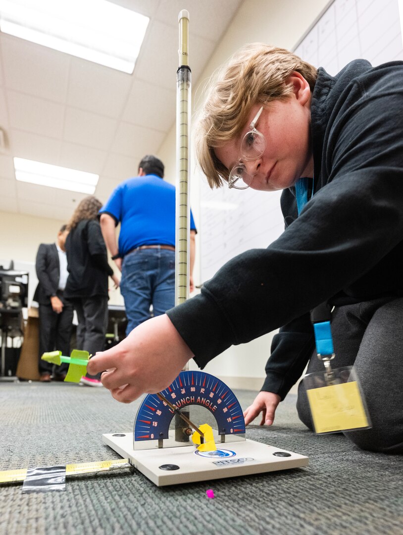 A boy kneels on the floor loading his rocket onto a launcher.