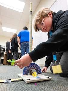 A boy kneels on the floor loading his rocket onto a launcher.