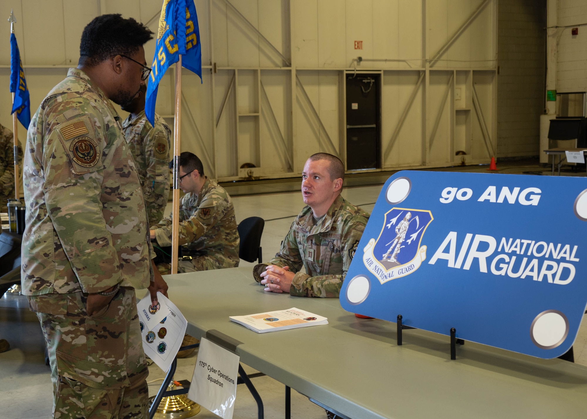 An airman of the Maryland Air National Guard speaks with a member of the 175th Cyber Operations Squadron during the first day of the 175th Wing Resource Fair at Warfield Air National Guard Base at Martin State Airport, Maryland, May 1, 2025. In response to the planned divestment of the A-10C Thunderbolt II aircraft and mission, each unit of the 175th Wing was represented and used interactive displays, kiosks and subject matter experts ready to explain their missions, as well as discuss opportunities for cross-training, benefits, bonus eligibility, save pay options and more. (U.S. Air National Guard Photo by Airman 1st Class Sarah Hoover)