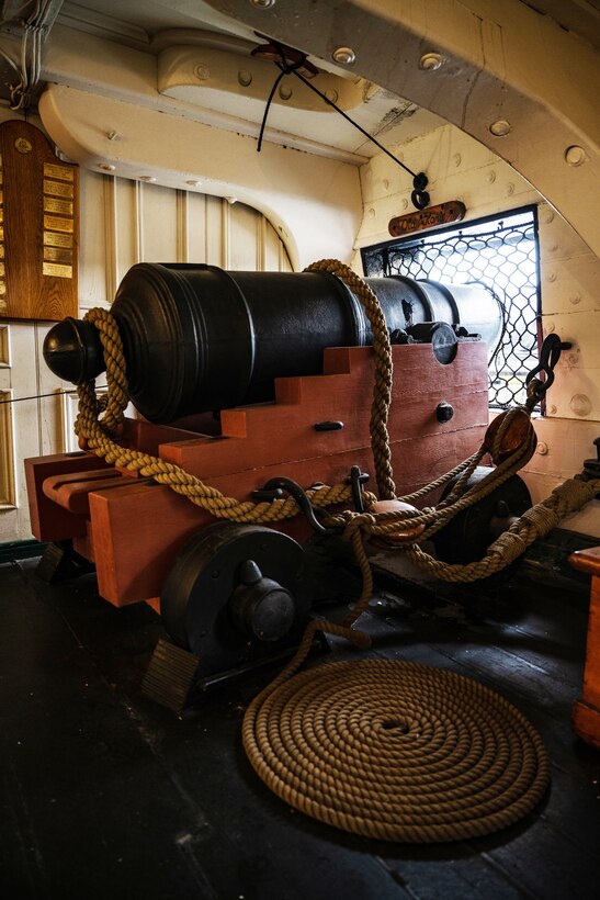 A canon is positioned next to a window aboard an old ship.