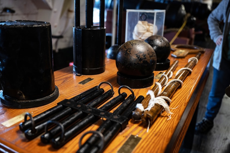 Various weapons rest atop a wooden desk aboard an old ship.