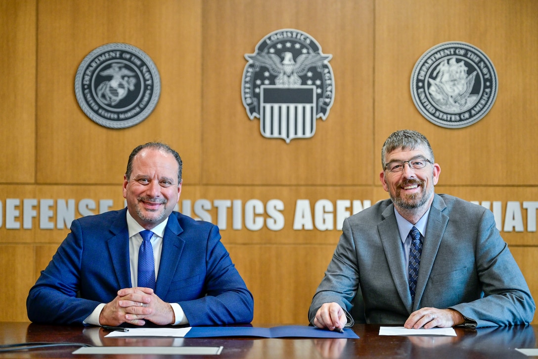 Two men are pictured with a partnership agreement in front of them.