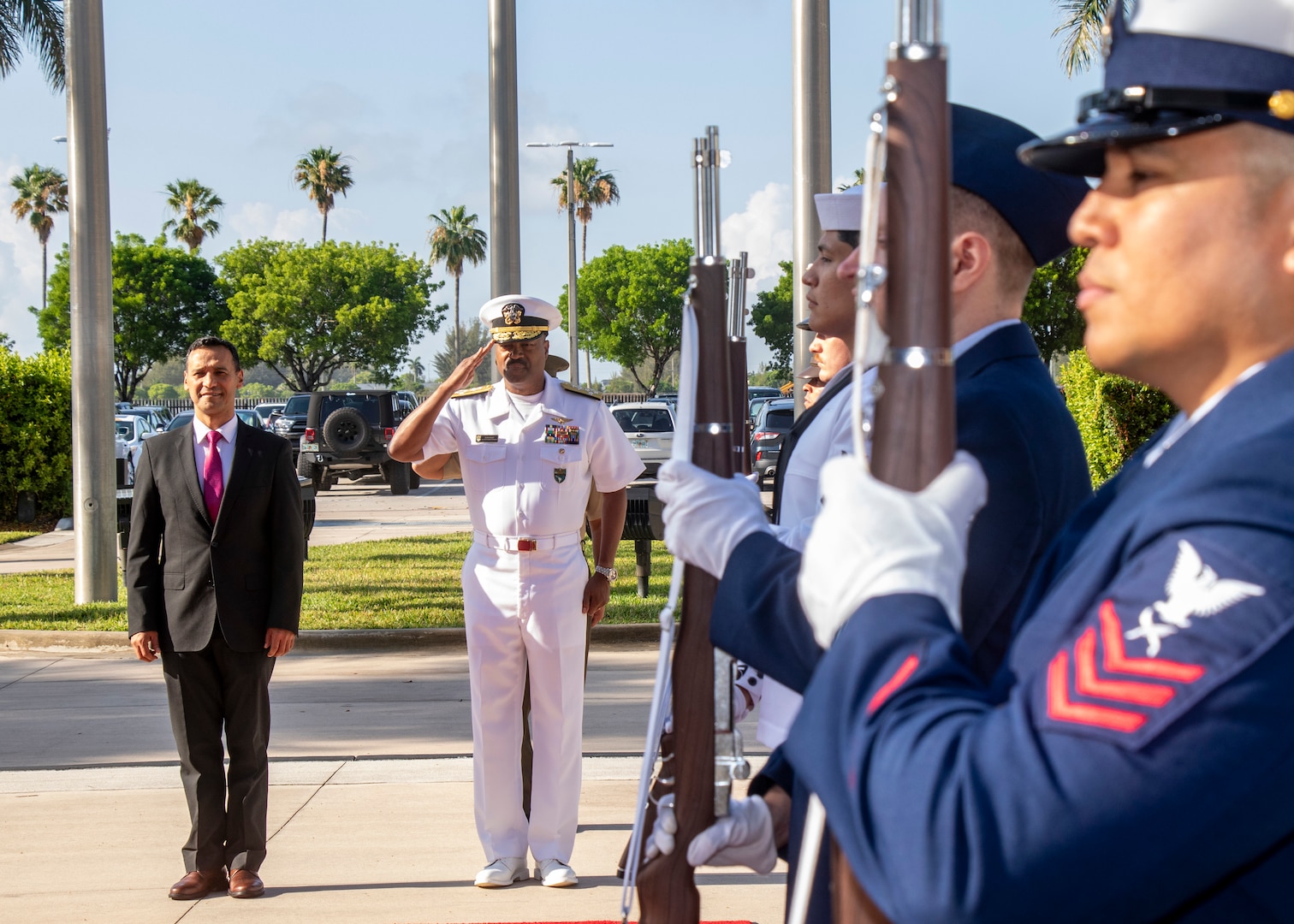 A man in a black suit stands alongside a man in a white uniform saluting.