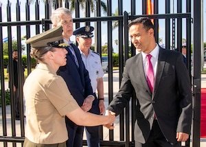 A woman in a military uniform shakes hands with a man in a black suit.