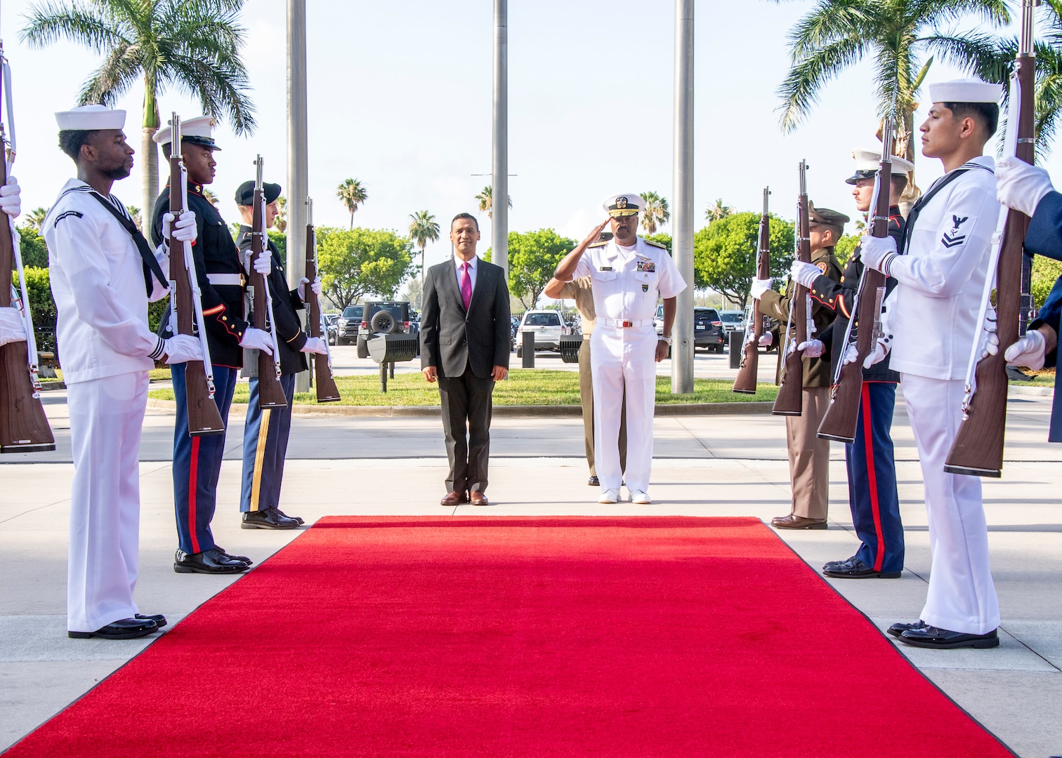 A man in a dark suit stands alongside a man in a white uniform saluting.