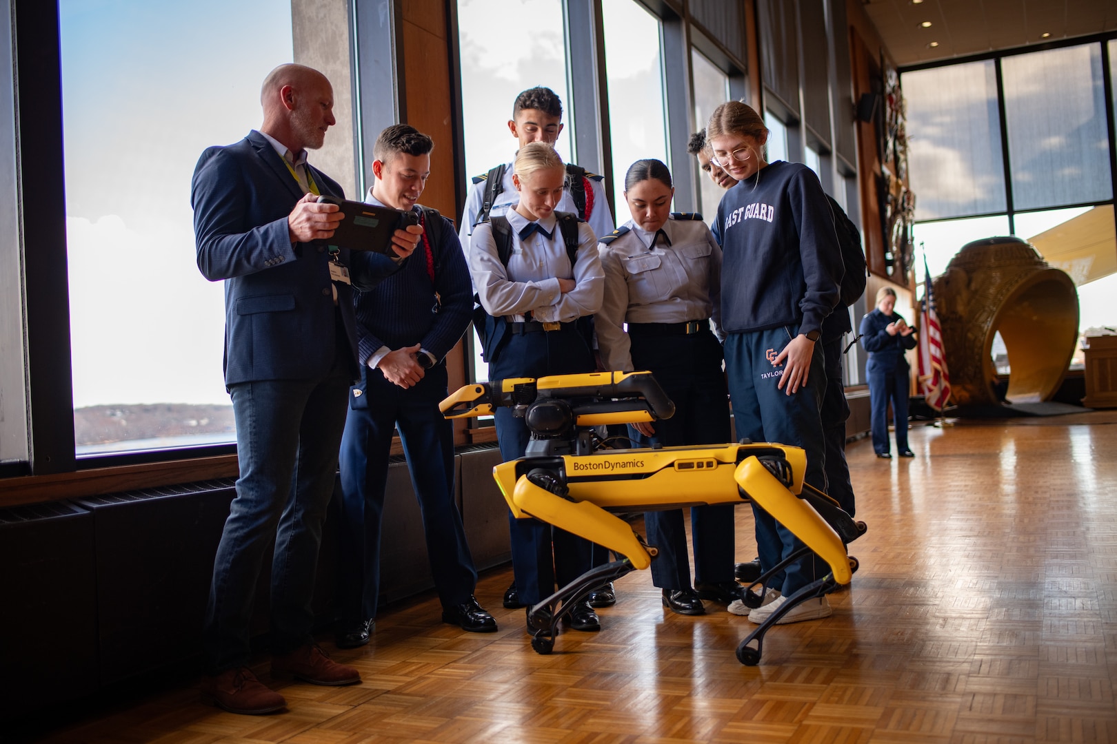 U.S. Coast Guard Academy (USCGA) cadets observe Boston Dynamic’s robot, Spot, controlled by a Massachusetts Institute of Technology (MIT) Lincoln Laboratory researcher (left) at USCGA, New London, Connecticut, Nov. 27, 2023. MIT’s Lincoln Laboratory showcased Spot and its functions to cadets, faculty, and staff. (Photo by U.S. Coast Guard Petty Officer Third Class Matthew Thieme.)