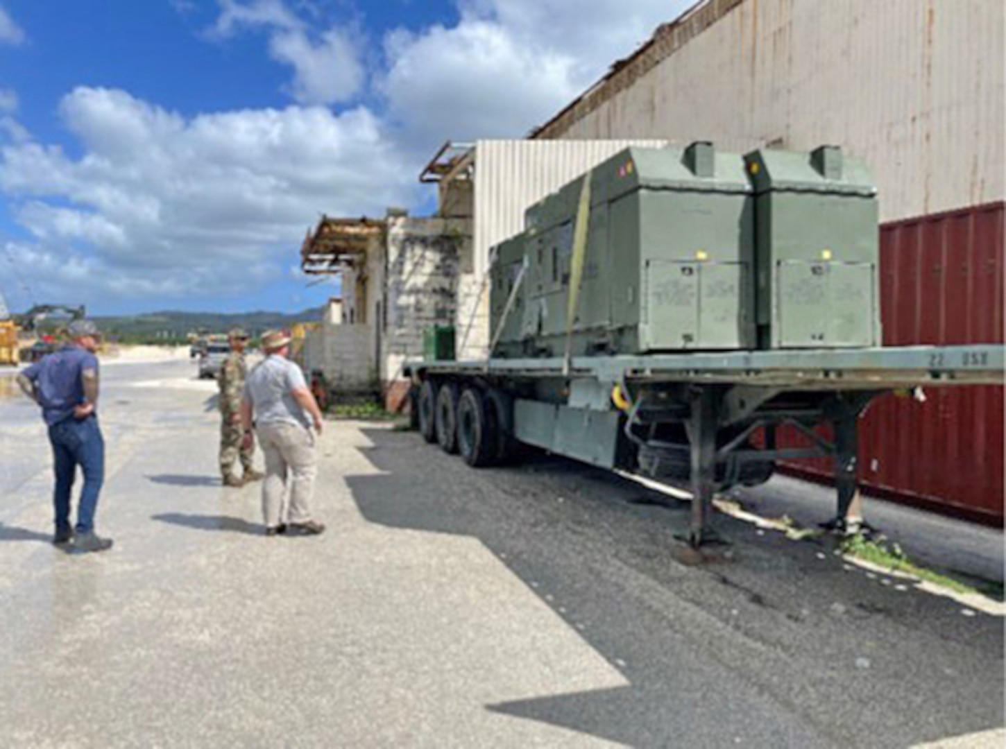 Men look at large generators on a flatbed trailer outside a warehouse.