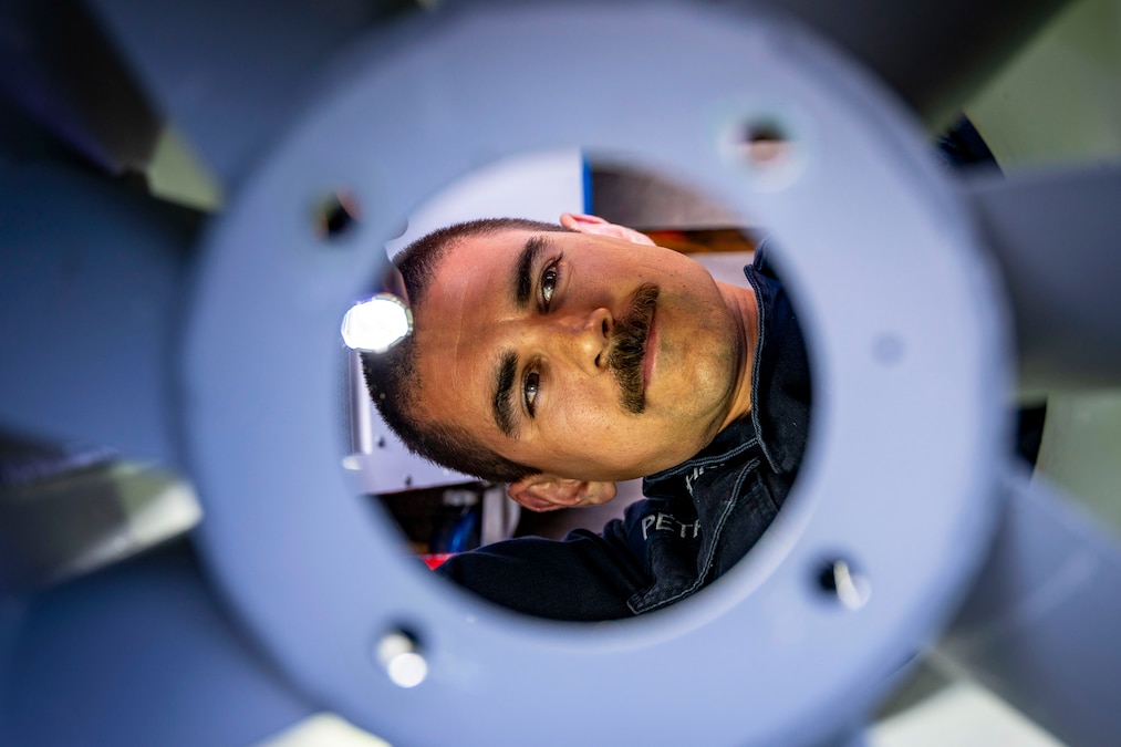 A sailor uses a flashlight to inspect fan blades.