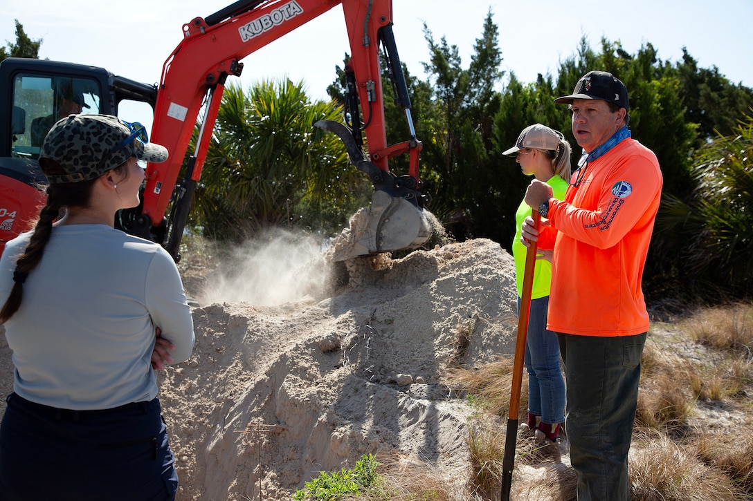 Taylor Comstock, Marine Corps environmental protection specialist, discusses gopher tortoises with Dave Yow, an Environmental Resource Solutions wildlife biologist, while Betsy Stewart, an environmental scientist, watches a burrow excavation during a survey May 2, 2025, along the St. Johns River at Marine Corps Support Facility Blount Island, Florida. (Official U.S. Marine Corps Photo/Dustin Senger)