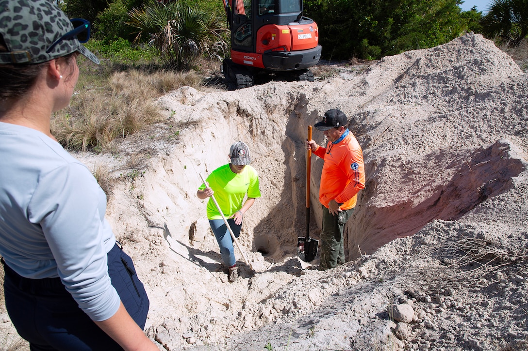 Taylor Comstock, Marine Corps environmental protection specialist, watches Betsy Stewart, an Environmental Resource Solutions environmental scientist, and Dave Yow, a wildlife biologist, excavate a burrow during a survey May 2, 2025, along the St. Johns River at Marine Corps Support Facility Blount Island, Florida. (Official U.S. Marine Corps Photo/Dustin Senger)