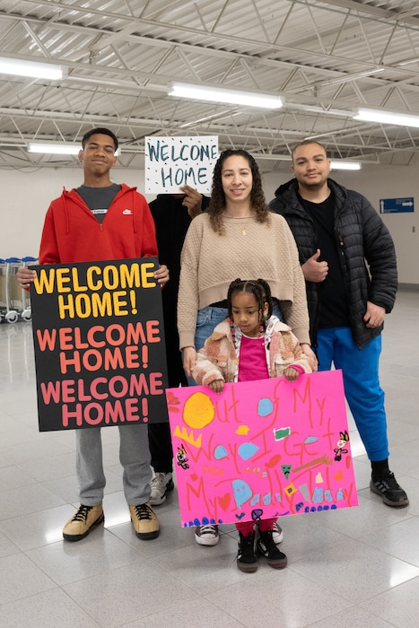 a family poses holding signs to welcome their family member home from deployment