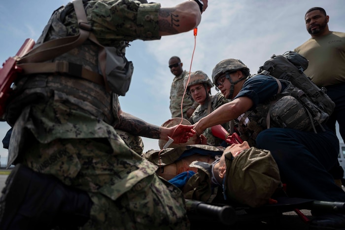 Military medical professionals perform medical care on a mannequin.