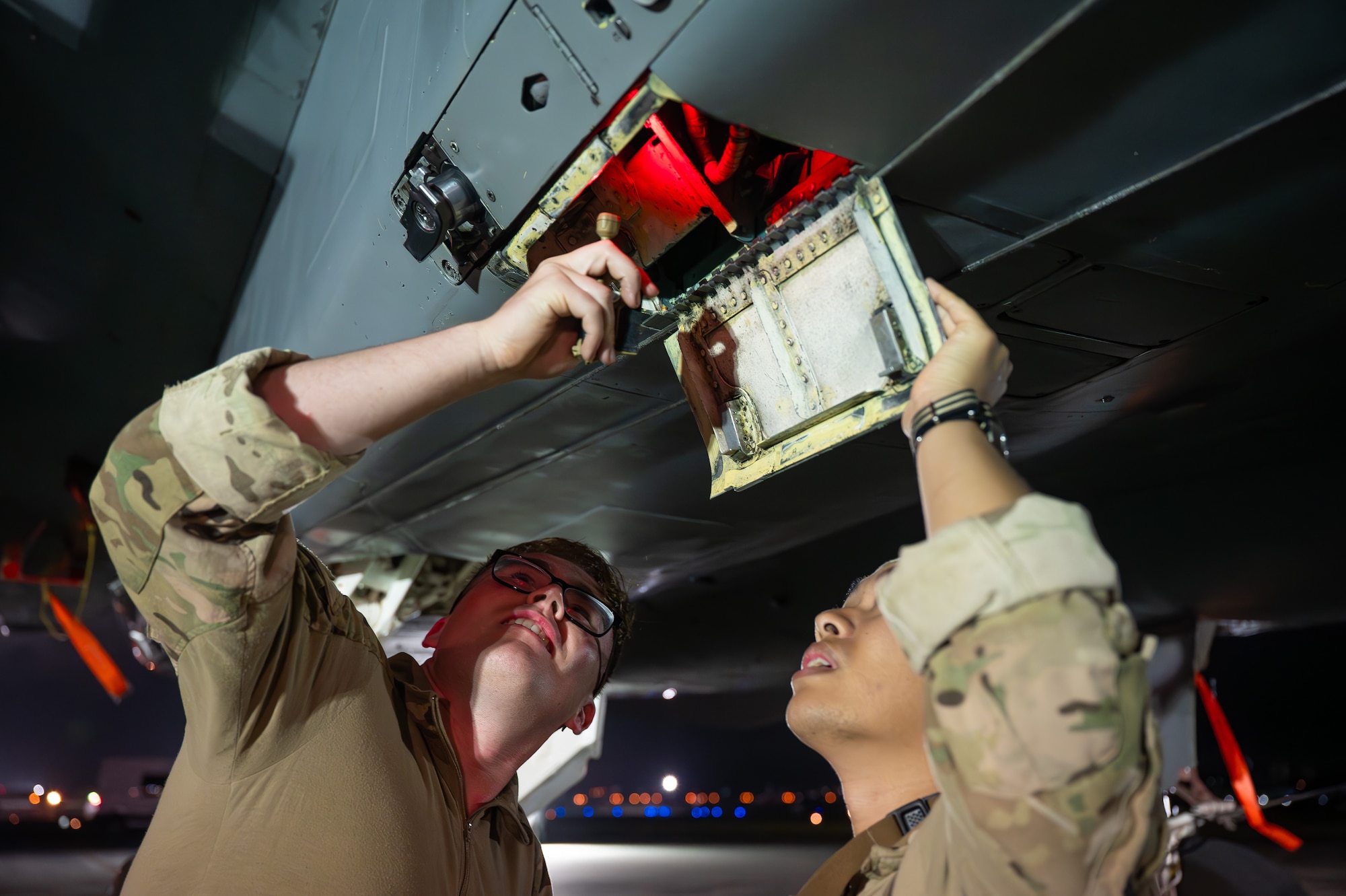 Service members service an aircraft at night.