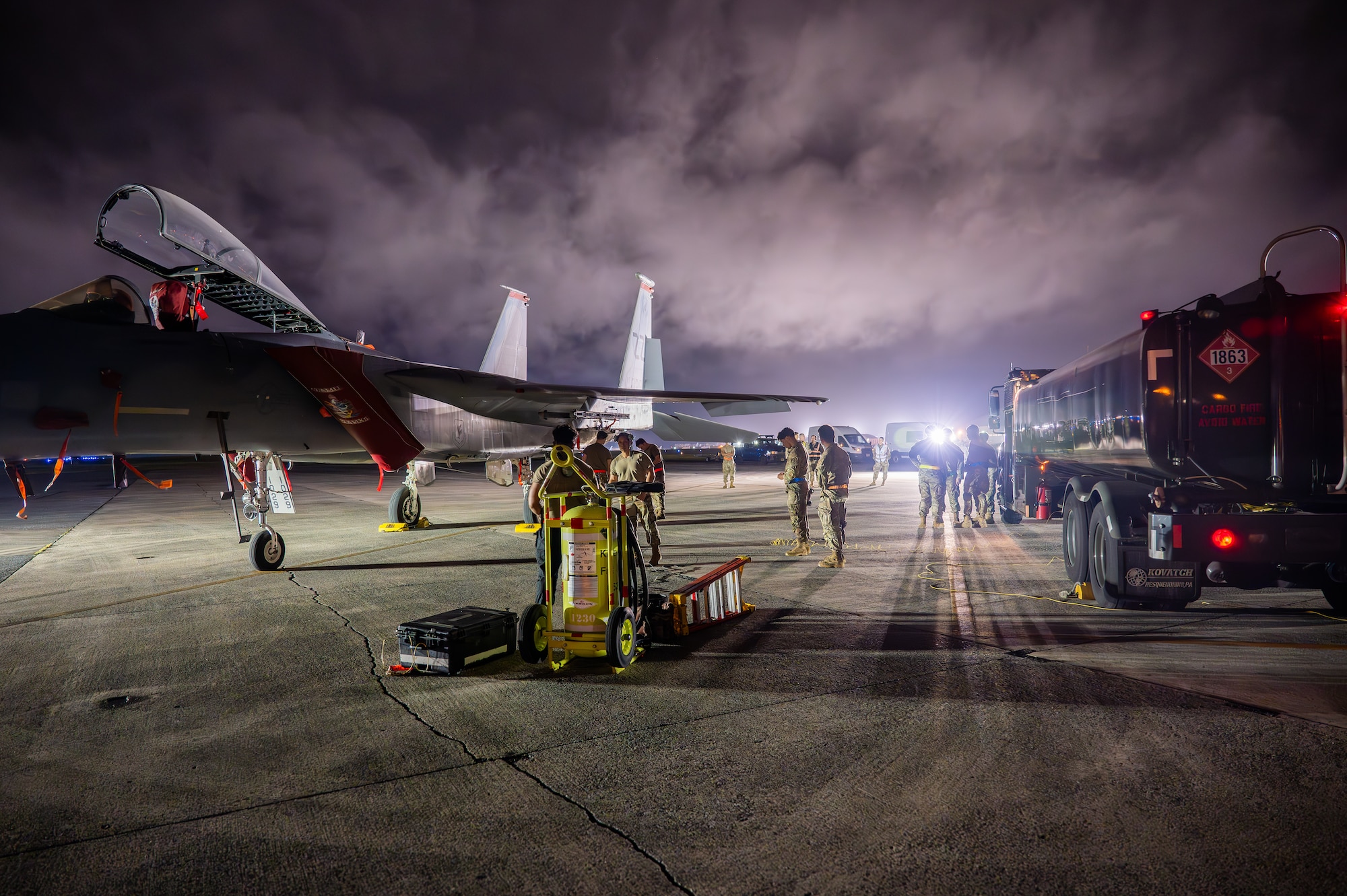 Service members service an aircraft at night.
