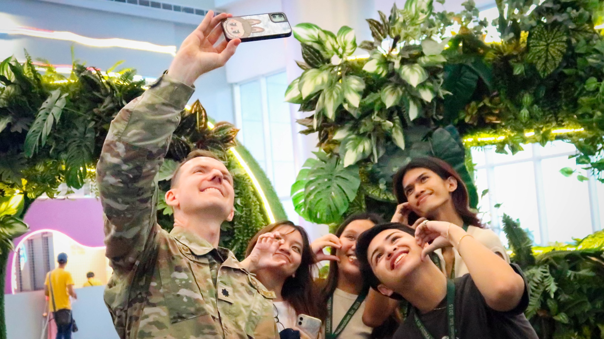 A man in military uniform takes a selfie with several civilians.