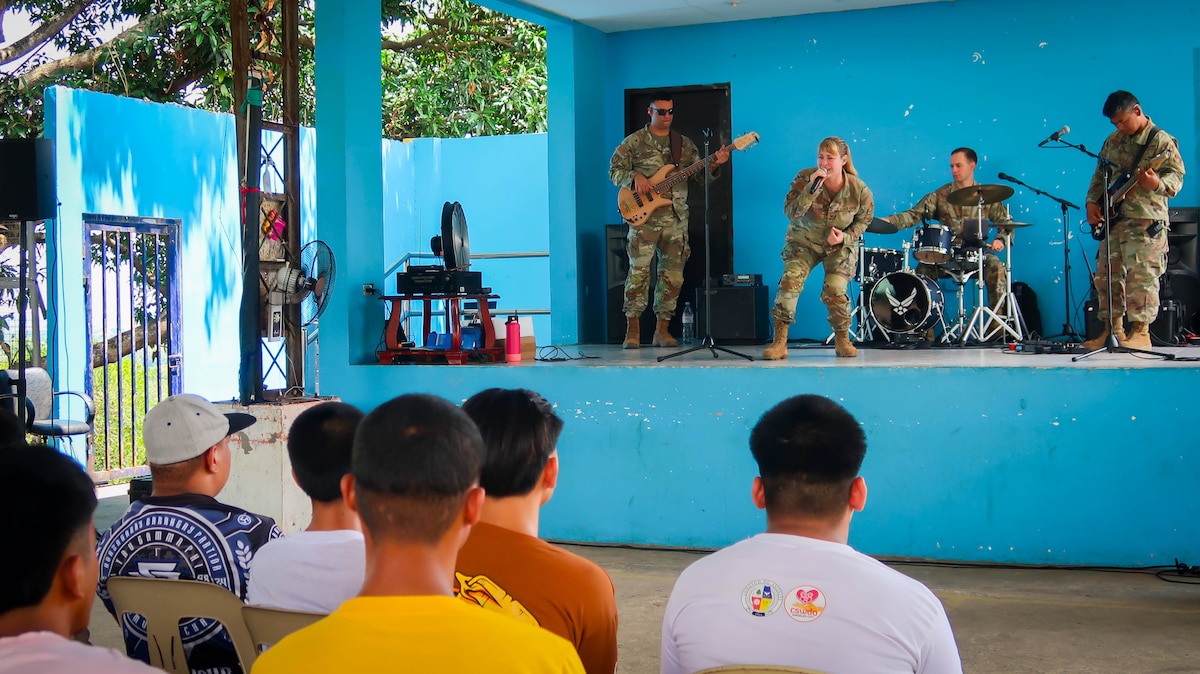 A four member band in military uniforms plays for a small group of teenagers