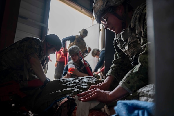 A military member applies pressure to a bandage on a simulated patient.