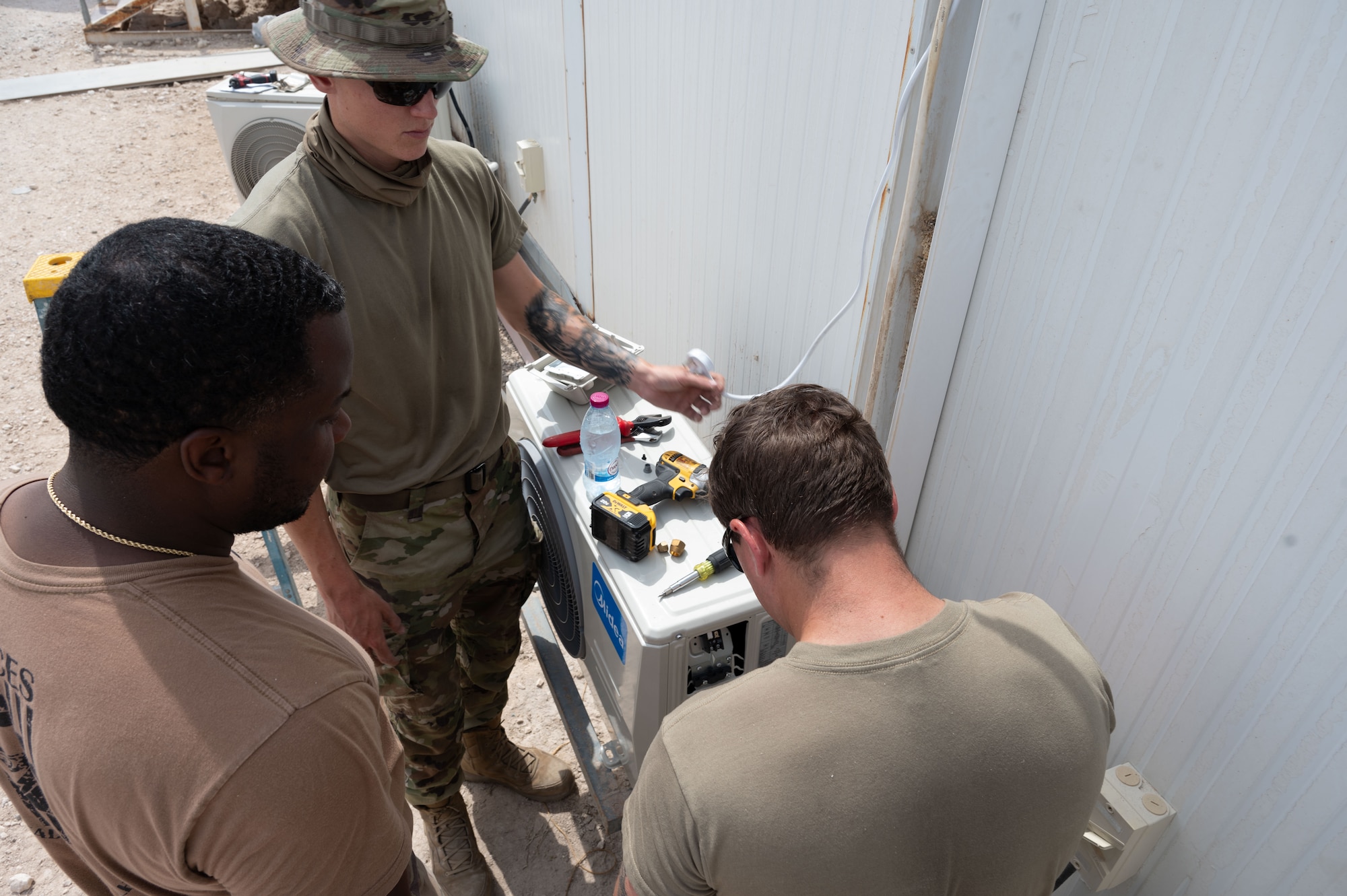 U.S. Air Force Senior Airman Gannon Cassey, left, 379th Expeditionary Civil Engineer Squadron heating ventilation and air conditioning journeyman, Staff Sgt. Dorian Brooks, middle, 379th ECES HVAC craftsman, middle, and Senior Airman Dylan Harris, ECES HVAC specialist, take apart an AC unit for installation within the U.S. Central Command area of responsibility, April 26, 2025. The HVAC team installed air conditioning units in preparation for the summer heat. (U.S. Air Force photo by Senior Airman Dieondiere Jefferies)