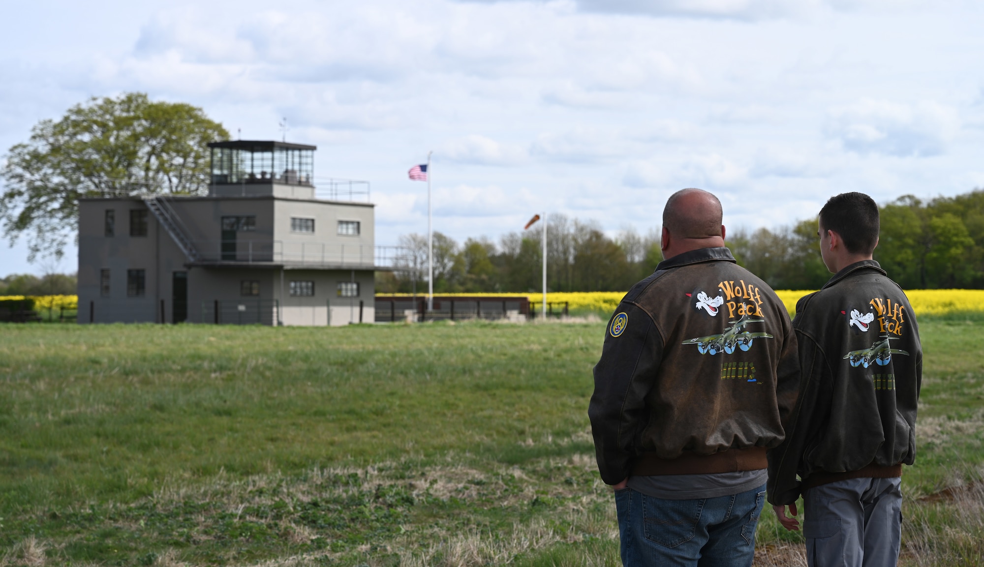 Randy Wolff, left, grandson of Capt. Robert “Bob” Wolff, World War II and 100th Bomb Group veteran, and his son Austin, great-grandson of the veteran, gaze emotionally at the control tower after walking the taxiway and hardstands at the former World War II air base at Thorpe Abbotts, England, April 16, 2025. Five of Bob Wolff’s family members visited Thorpe Abbotts from California and North Carolina to lay his ashes to rest and bring the former B-17 Flying Fortress pilot “home.” He had previously never returned after his eighth mission due to becoming a prisoner-of-war at Stalag-Luft III, Germany. (U.S. Air Force photo by Karen Abeyasekere)