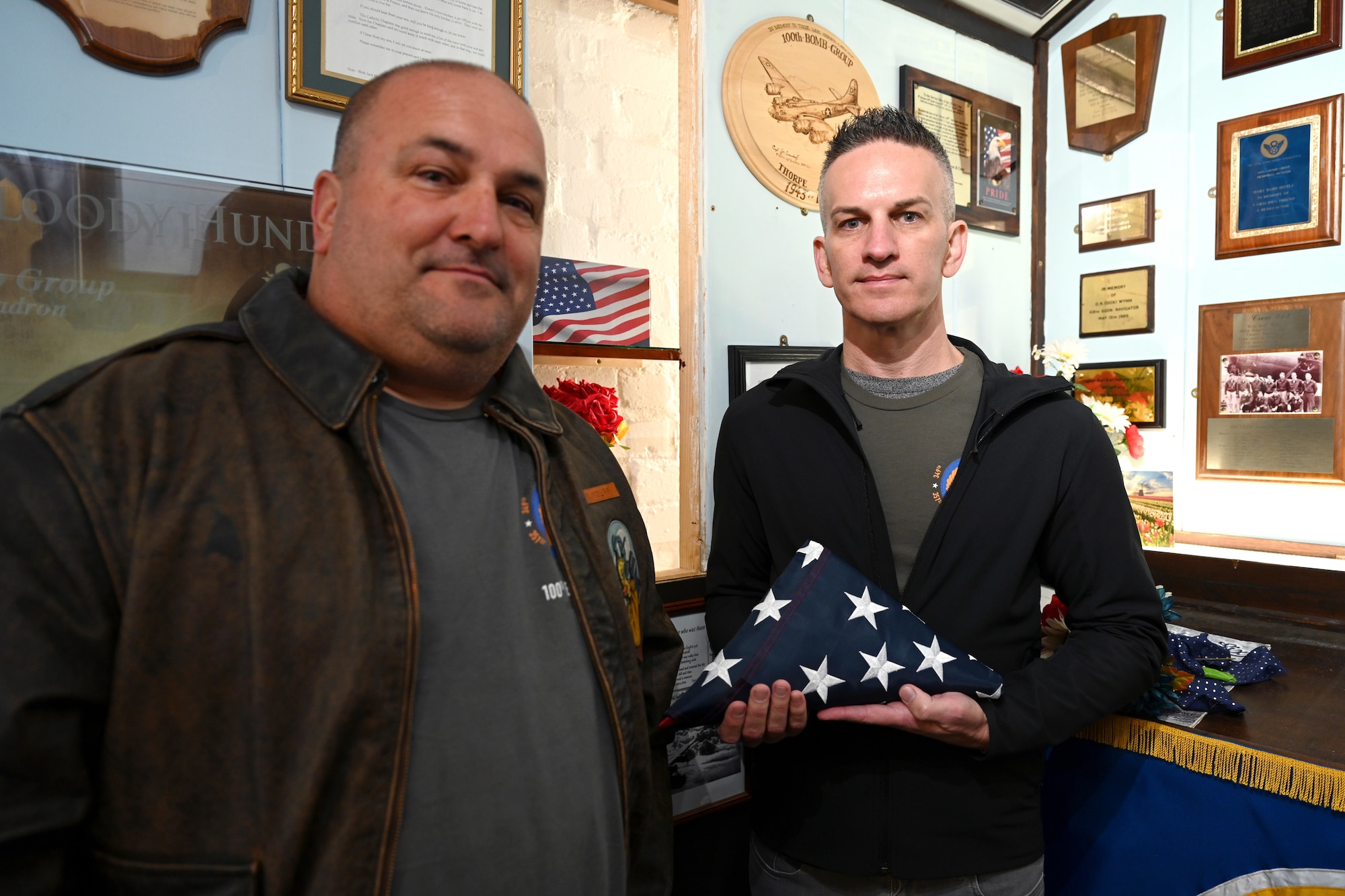 Randy Wolff, left, and Jeffrey Paul Wolff, both grandsons of World War II and 100th Bomb Group veteran Capt. Robert “Bob” Wolff, stand by their grandfather’s ashes as they hold a flag presented to them by the RAF Mildenhall Honor Guard at Thorpe Abbotts, England, April 16, 2025. Capt. Wolff was a B-17 Flying Fortress pilot and passed away in October 2024 at age 103. He had previously never returned after his eighth mission due to becoming a prisoner-of-war at Stalag-Luft III, Germany. (U.S. Air Force photo by Karen Abeyasekere)
