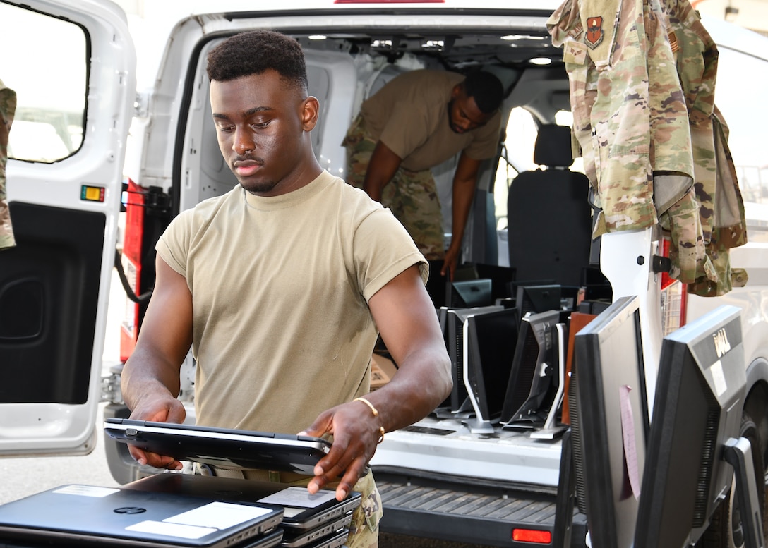 A man in a tan T-shirt stacks laptops