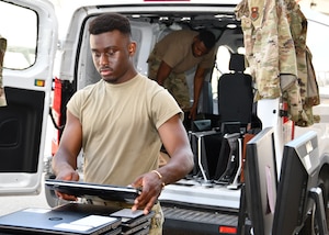 A man in a tan T-shirt stacks laptops