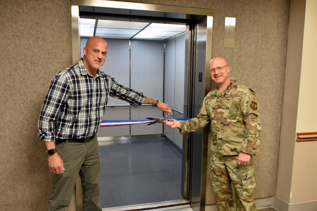 Col. Eric Withrow, Arnold Engineering Development Complex Test Support Division chief, right, and Joseph Baxter, project manager, prepare to cut the ribbon on the new elevator in the Administration and Engineering Building at Arnold Air Force Base, Tenn., May 5, 2025. Arnold AFB is the headquarters of AEDC. The process of replacing the elevator was a two-year effort overseen by the AEDC Civil Engineering Branch. The previous elevator had been in place since construction of the building and was originally intended to serve as a cargo elevator. (U.S. Air Force photo by Bradley Hicks)