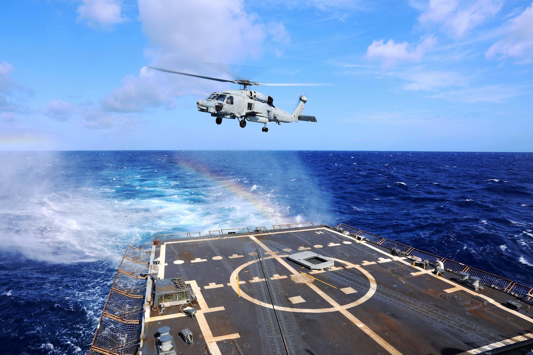 A military helicopter takes off from the deck of a ship at sea.