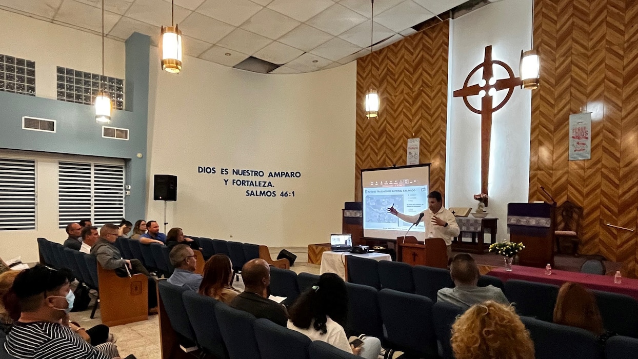 People in a room watching a man share a presentation on a large screen.