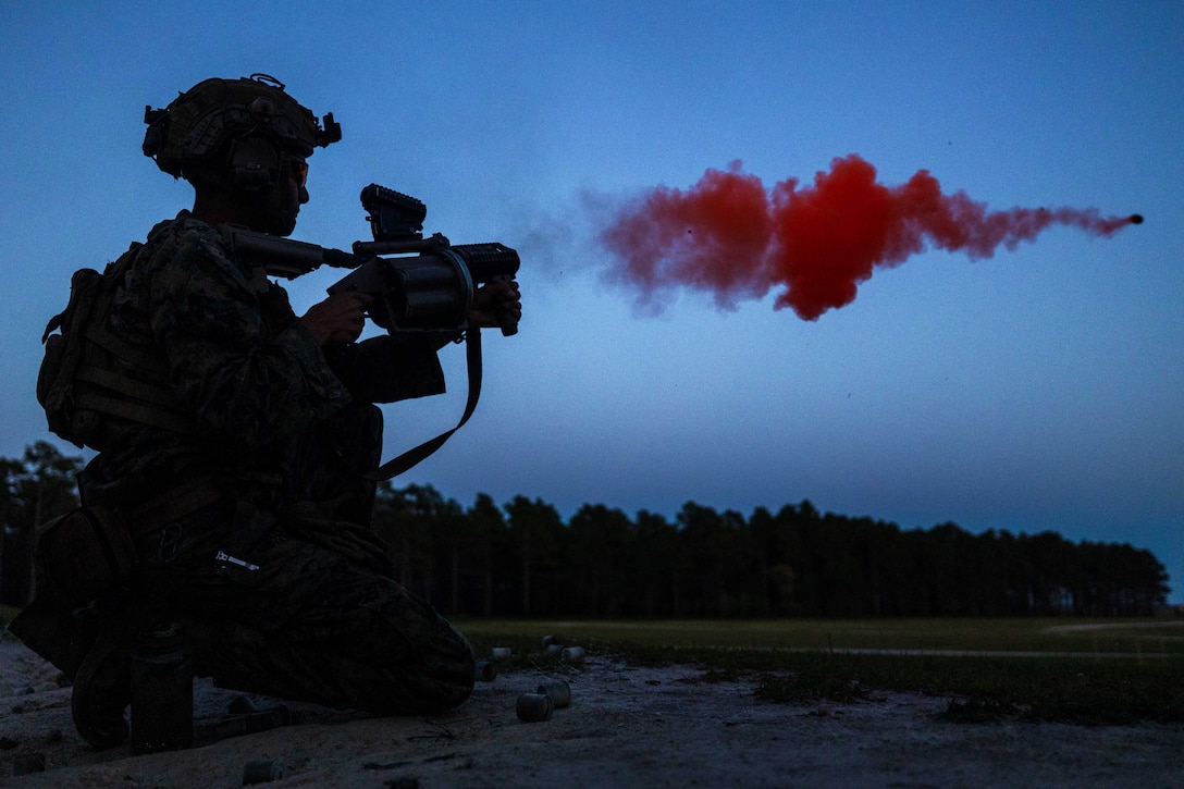 A kneeling Marine fires a weapon that leaves a red, smoky trail behind the grenade it launched.