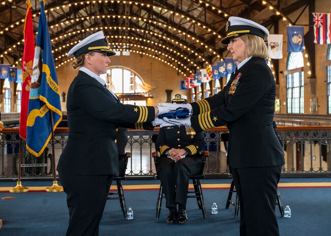 (250411-N-IX644-1017) ANNAPOLIS, Md. Cmdr. Aldebaran Imperatore presents Capt. Lydia Doye, a folded American flag  during the reading of “Old Glory” during Doye’s retirement ceremony in Dahlgren Hall at the United States Naval Academy, April 11, 2025. Capt. Doye served in the Navy for 27 years, building, training, and developing Sailors as a pilot and later as a human resources officer. (U.S. Navy photo by Mass Communication Specialist 2nd Class Sasha Ambrose)