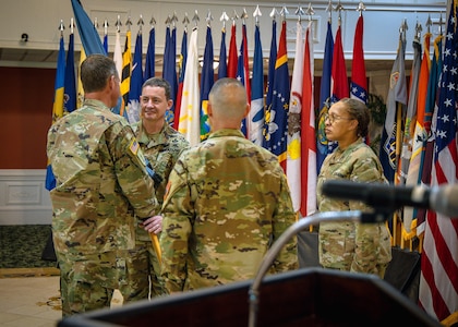 Newly designated Command Sergeant Major Timothy McGuire accepts the unit colors as outgoing CSM Michael Starrett and G-3 Sergeant Major Nicola Felder look on during the Change of Responsibility ceremony at the Eisenhower Conference and Catering Center April 16, 2025.