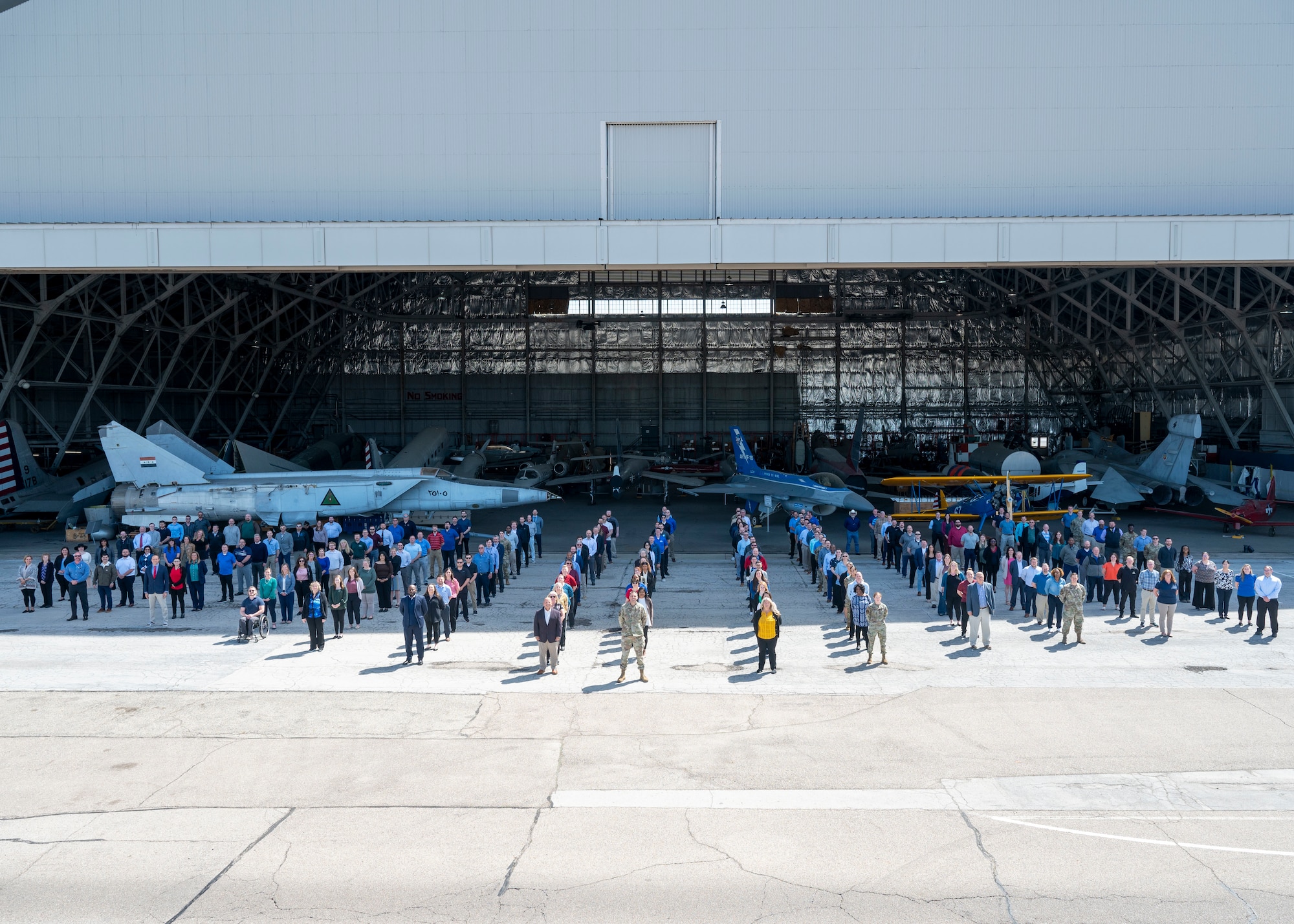 Group of people in front of airplane hangar. 