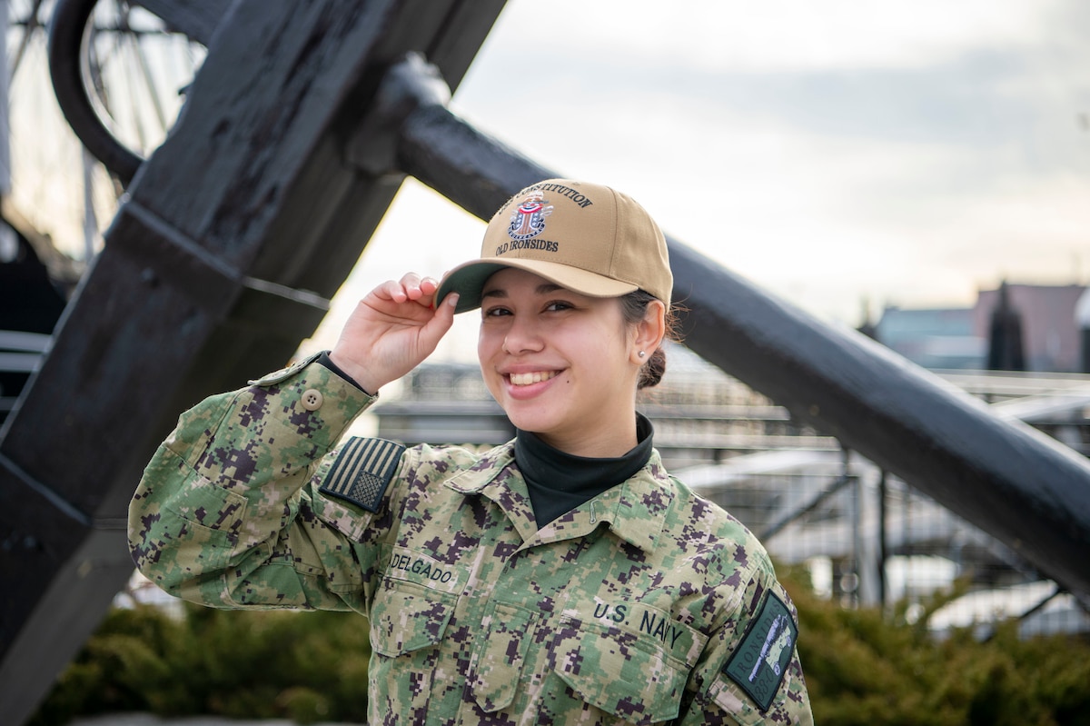 A sailor holds their baseball cap while smiling for the picture.