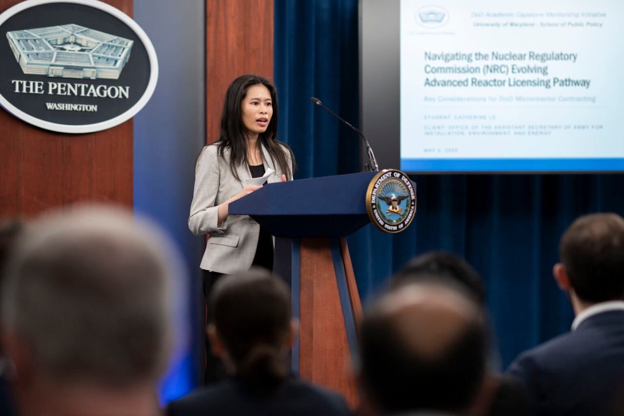 A woman stands at a lectern and speaks to a seated crowd.