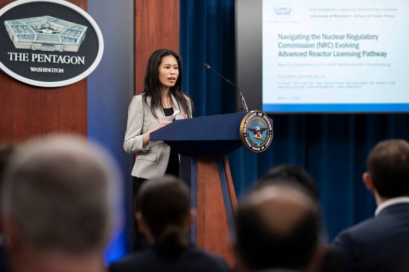 A woman stands at a lectern and speaks to a seated crowd.