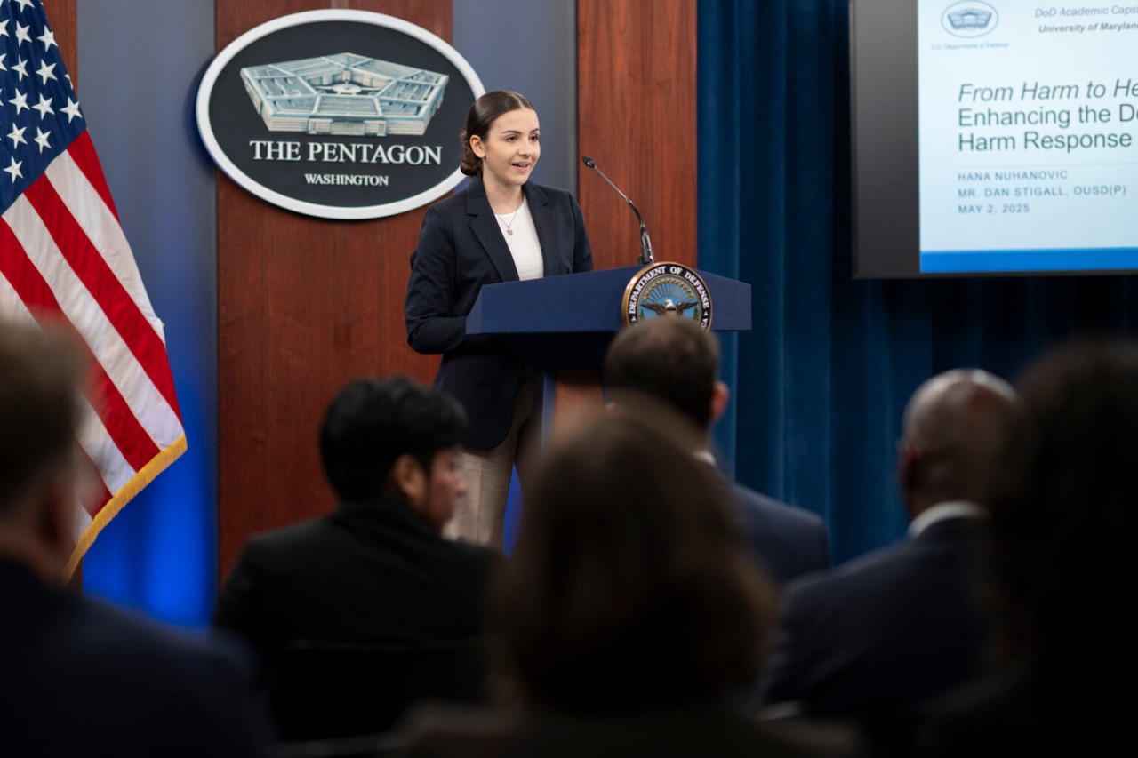 A woman stands at a lectern and speaks to a seated crowd.
