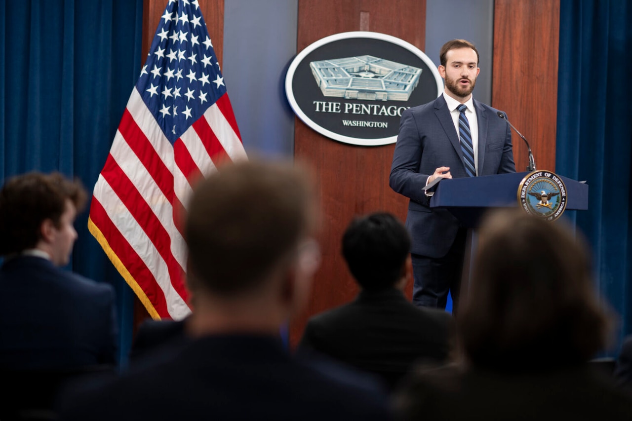 A man stands at a lectern and speaks to a seated crowd.