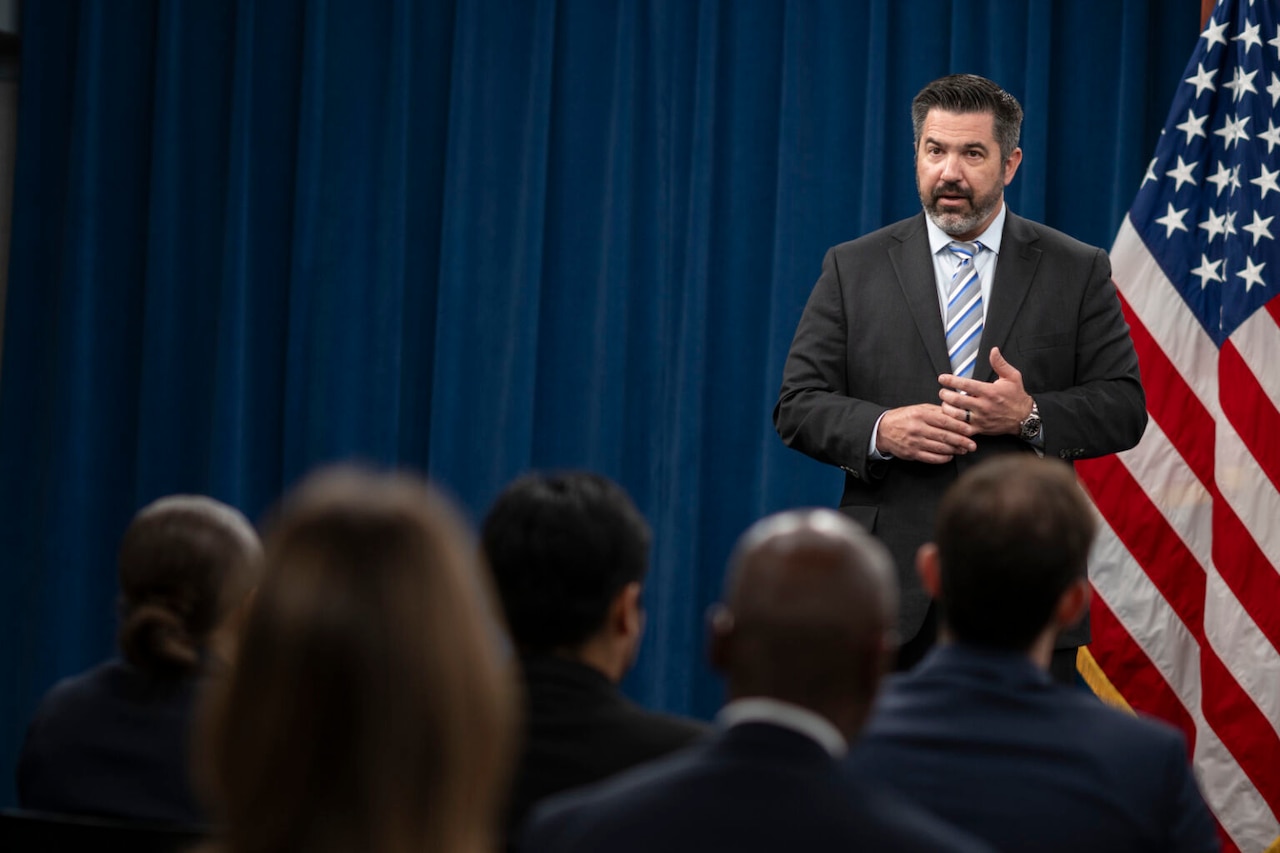 A man speaks to a seated group of people.